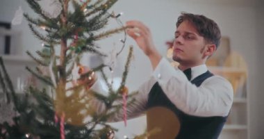 İyi giyimli genç adam evdeki Noel ağacına ışık tutuyor.