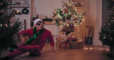 Heyecanlı genç adam, Noel boyunca aydınlatılmış evde dans ederken dublörlük yapıyor.