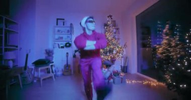 Noel Baba şapkalı ve güneş gözlüklü genç adam Noel 'de aydınlatılmış evde parti sırasında hızla performans sergiliyor.