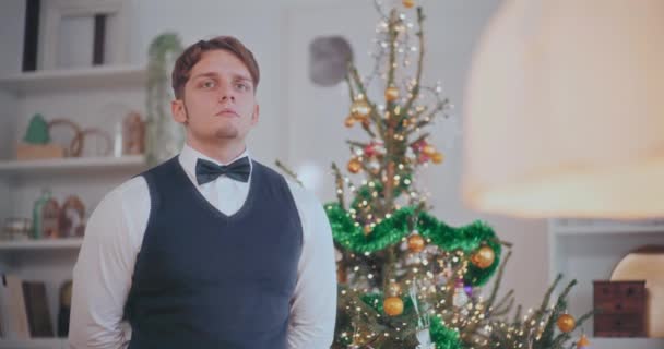 自宅で装飾されたクリスマスツリーで立っている間 タキシードの熟練した服を着た若者 — ストック動画