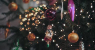 Erkek eli evdeki aydınlanmış Noel ağacına kırmızı parlak bir mücevher asıyor.
