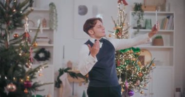 İyi giyimli genç adam, Noel boyunca evde dijital tablette görüntülü konuşma yaparken el kol hareketi yapıyor.
