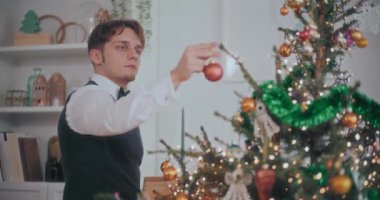 Genç, yakışıklı, iyi giyimli adam evdeki aydınlanmış Noel ağacına takılıyor.