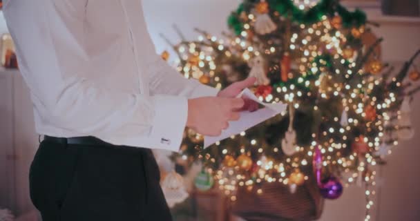 自宅で背景に装飾されたクリスマスツリーと立っている間 フォームを開く男性のミックス — ストック動画