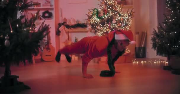 エキサイティングな若者はクリスマスの間に装飾された家で床で踊りながらスタントを行います — ストック動画