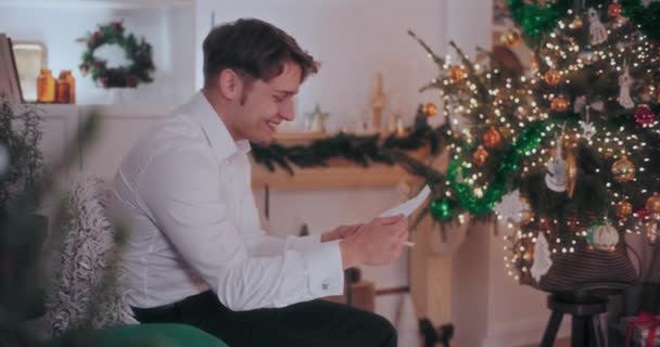 Oldalnézet Boldog Fiatalember Olvas Levelet Miközben Széken Díszített Otthon Karácsonykor — Stock videók
