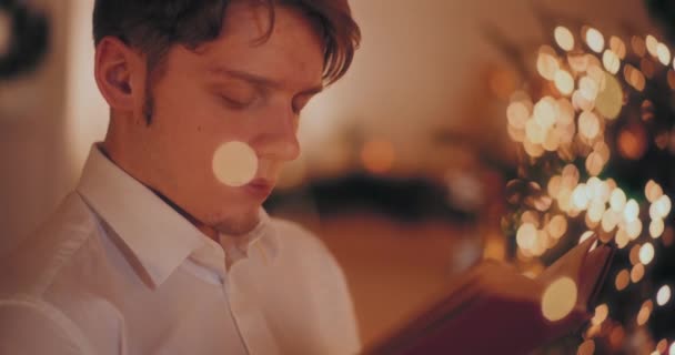 Молодой Человек Читает Роман Сидя Освещенном Доме Время Рождества — стоковое видео