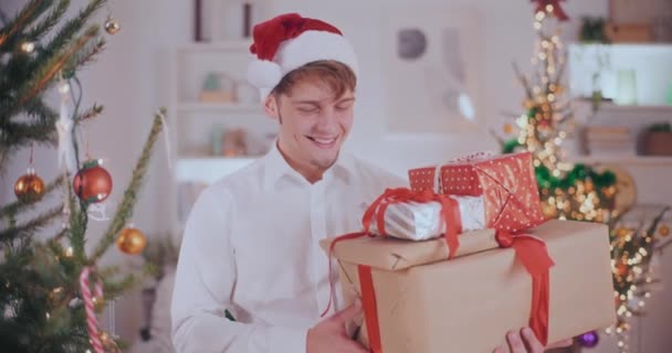 Retrato Jovem Bonito Chapéu Santa Sorrindo Enquanto Carrega Vários Presentes — Vídeo de Stock