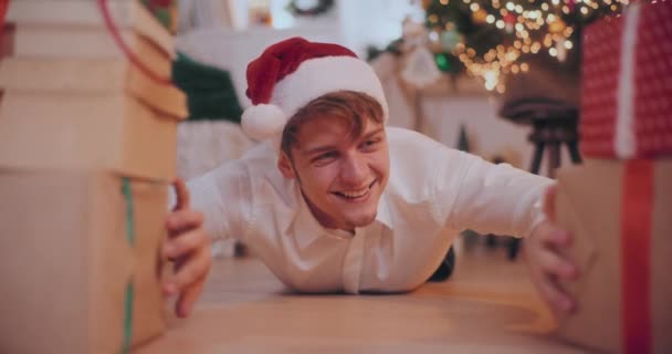 집에서 바닥에 누워있는 크리스마스 선물을 슬라이딩 모자에 놀라운 남자의 초상화 — 비디오
