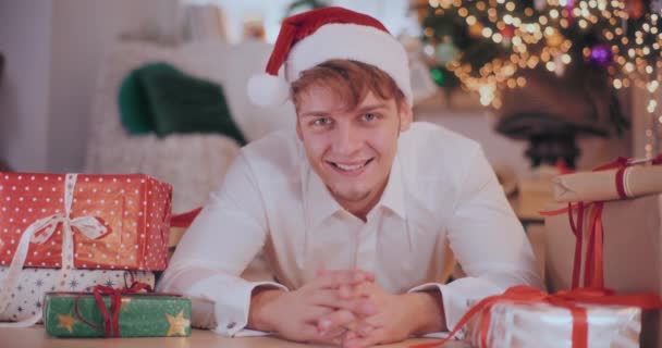 Portrét Šťastného Mladého Muže Santa Klobouk Ležící Podlaze Vánočními Dárky — Stock video