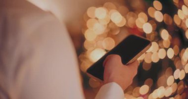 Noel 'de aydınlatılmış evde akıllı telefon kullanan kırpılmış erkek eli.