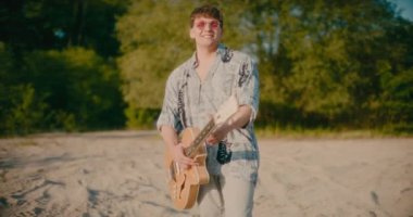 Olumlu gitarist elinde gitar tutuyor açık havada gitar çalıyor dans ediyor ve yürüyor.