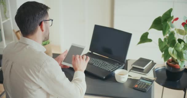 年轻的男性企业家在办公室里坐着和工作时 用数字平板电脑和笔记本电脑完成多项任务 — 图库视频影像