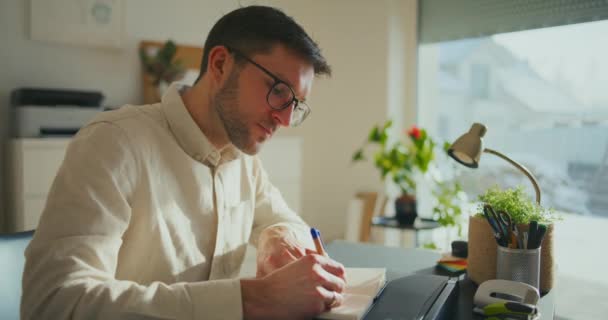 以男性企业家为重点 坐在办公桌前 戴着眼镜 在书中写下自己的商业理念 — 图库视频影像