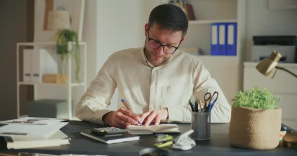 オフィスのデスクで日記を書いている間の戦略を準備する不思議な男性起業家 — ストック動画