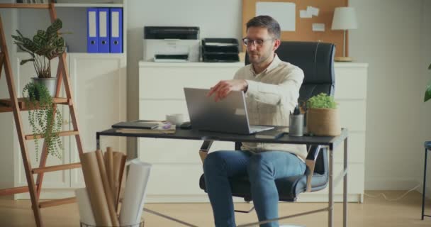 年轻的男性商业专家坐在办公室的办公桌前 一边用笔记本电脑开始工作 — 图库视频影像