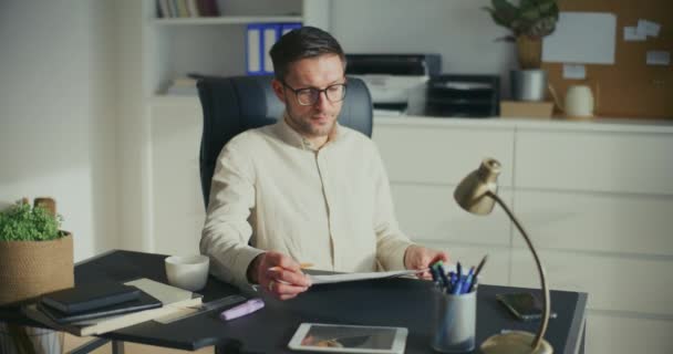オフィスの机に座っている間青写真を検査する若い男性ビジネス専門家 — ストック動画