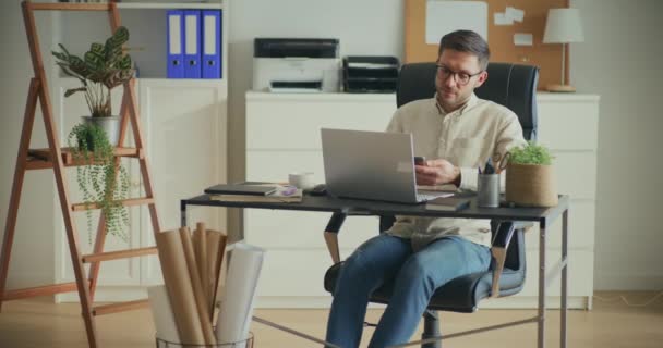 Mannelijke Ondernemer Met Behulp Van Smartphone Werken Laptop Terwijl Zitten — Stockvideo