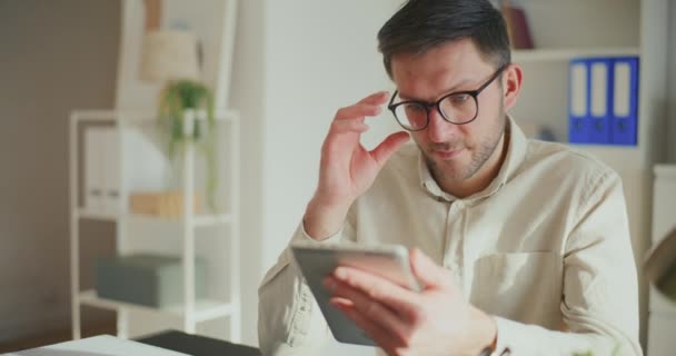 Jovem Empresário Ajustando Óculos Usando Tablet Digital Enquanto Sentado Mesa — Vídeo de Stock