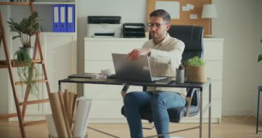 Genç erkek iş adamı ofiste otururken dizüstü bilgisayarda çalışmaya başlıyor.