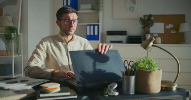 年轻的男性创业者一边打开笔记本电脑 一边坐在办公室的办公桌前开始工作 — 图库视频影像