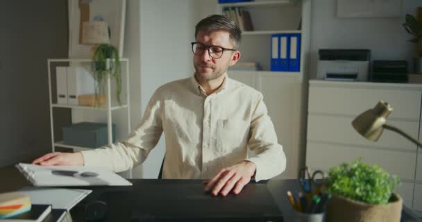 若い男性起業家がレポートを調べ オフィスの机に座ってノートパソコンで作業する — ストック動画