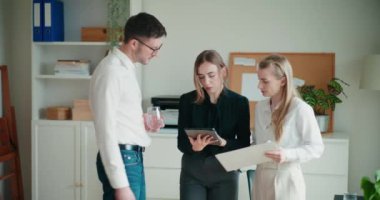 Şirket ofisindeki toplantı sırasında planlama yaparken belge ve dijital tablet üzerinde tartışan genç meslektaşlar