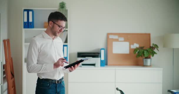 企業オフィスに立っている間 スタイラスでデジタルタブレットを使用している自信のある若いビジネスマン — ストック動画