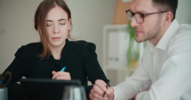 Genç iş kadını ve işadamı ofiste otururken dijital tablet üzerinden strateji tartışıyorlar