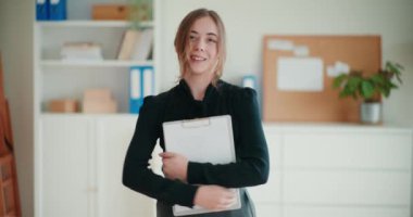 Şirketin çalışma alanında kolları çapraz dururken elinde bir pano tutan kendine güvenen genç iş kadınının portresi.