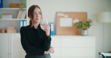 Şirketin işyerinde dururken elinde bir bardak su tutan gülümseyen genç iş kadını.