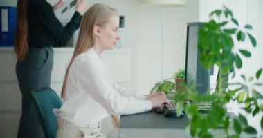 Şirket ofisindeki masada otururken bilgisayar kullanan kendine güvenen genç bir iş kadını.