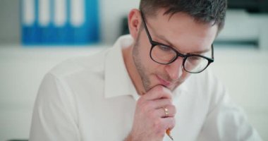 Şirket ofisinde çalışan, kendine güvenen, gözlüklü genç bir işadamı.