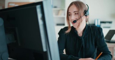 Kadın müşteri hizmetleri yöneticisi şirket ofisinde otururken kulaklıkla konuşuyor.