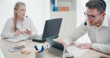 Genç işadamı, ofisteki meslektaşının yanındaki kağıt üzerinde strateji ve yazıları tartışırken kulaklıkla konuşuyor.