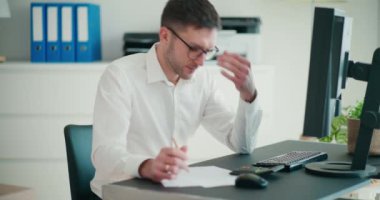 Stresli erkek girişimci şirket çalışma alanında bilgisayar masasında otururken bütçeyi hesaplıyor
