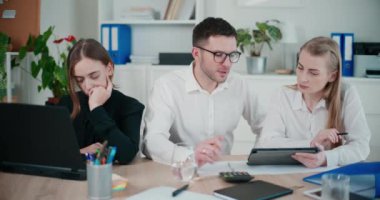 İş kadını, iş arkadaşlarının yanında oturup ofiste dijital tablet üzerinde tartışırken dizüstü bilgisayar kullanıyor.