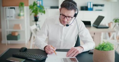 Genç işadamı ofiste kağıt üzerinde stratejiyi tartışırken kulaklıkla konuşuyor.