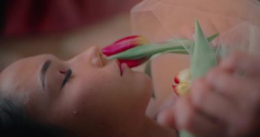 Baştan çıkarıcı genç bir kadının yatakta yatarken yüzüne çiçekle dokunuşunun yakın çekimi.