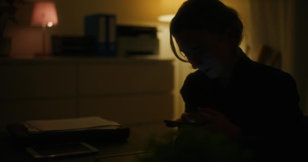 年轻的女企业家一边浏览互联网 一边在黑暗的工作空间里滚动智能手机 — 图库视频影像