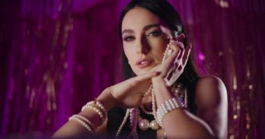 Arka planda dekorasyon yaparken inci kolye tutan baştan çıkarıcı, modaya uygun genç bir kadının portresi.