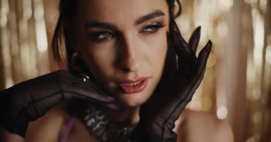 Siyah eldivenli, parlak dekorasyonun önünde poz veren çekici genç bir kadının yakın çekimi.