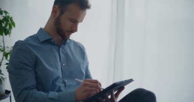 Stylus 'la birlikte iş yerinde otururken dijital tablet üzerinde kendine güvenen genç, sakallı girişimci erkek yazar stratejisi.