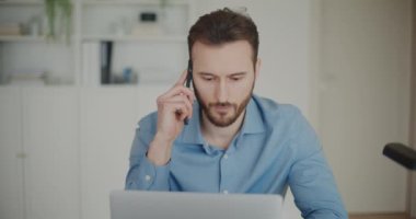 Ofiste dizüstü bilgisayarla otururken cep telefonuyla stratejiyi tartışan yakışıklı genç işadamı.