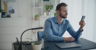 Akıllı telefonlu yakışıklı genç işadamının şirket işyerindeki masasında otururken çekilmiş kareleri.