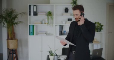 İş yerindeki akıllı telefondan aranarak stratejiyi tartışırken elinde bir pano tutan kendinden emin genç girişimci.