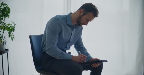 年轻自信的大胡子英俊商人坐在办公室的椅子上 用手写笔在数码平板电脑上书写策略 — 图库视频影像
