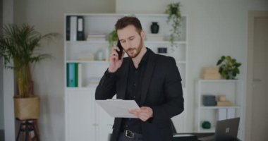 Kendine güvenen genç işadamı, şirket işyerindeki akıllı telefon aracılığıyla stratejiyi tartışırken pano tutuyor.