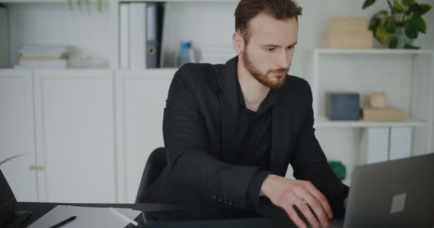 Stock video Worried young businessman using laptop while sitting with head in hands at office desk