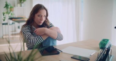 Oturma odasında dijital tabletle oturmuş, kafasını kaşıyarak düşünen genç bir kadının tecrit görüntüsü.